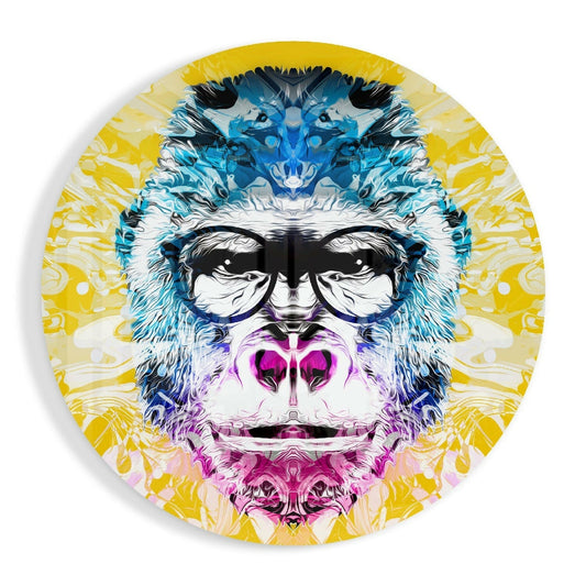 Circular glass wall art featuring a stylized primate face with blue, pink, and yellow colorwork and large black-rimmed glasses.