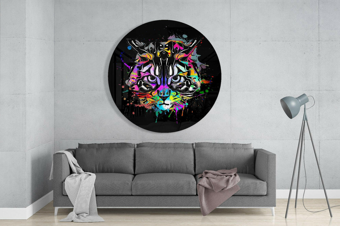 Colorful graffiti-style cat artwork on black circular canvas hanging above gray sofa in minimalist interior setting.
