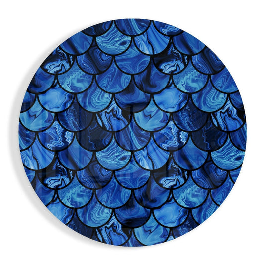 Circular glass wall art featuring overlapping blue and teal marble-patterned scales with black outlines, photographed straight-on against white background.