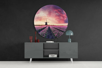 Circular glass wall art displaying purple tulip field with windmill at sunset, mounted above grey sideboard with red candles and teal lamp.