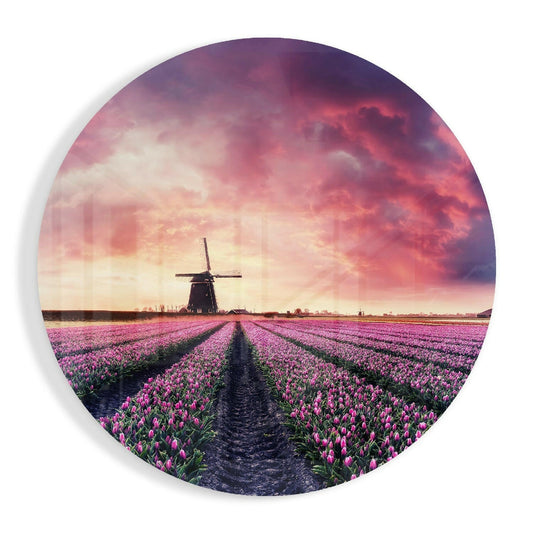 Circular glass wall art showing straight rows of pink tulips leading to a traditional windmill under a dramatic sunset sky.