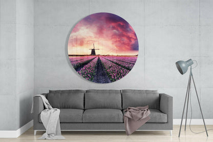 Circular glass wall art depicting purple tulip field with windmill at sunset, displayed above gray sofa in modern living room.