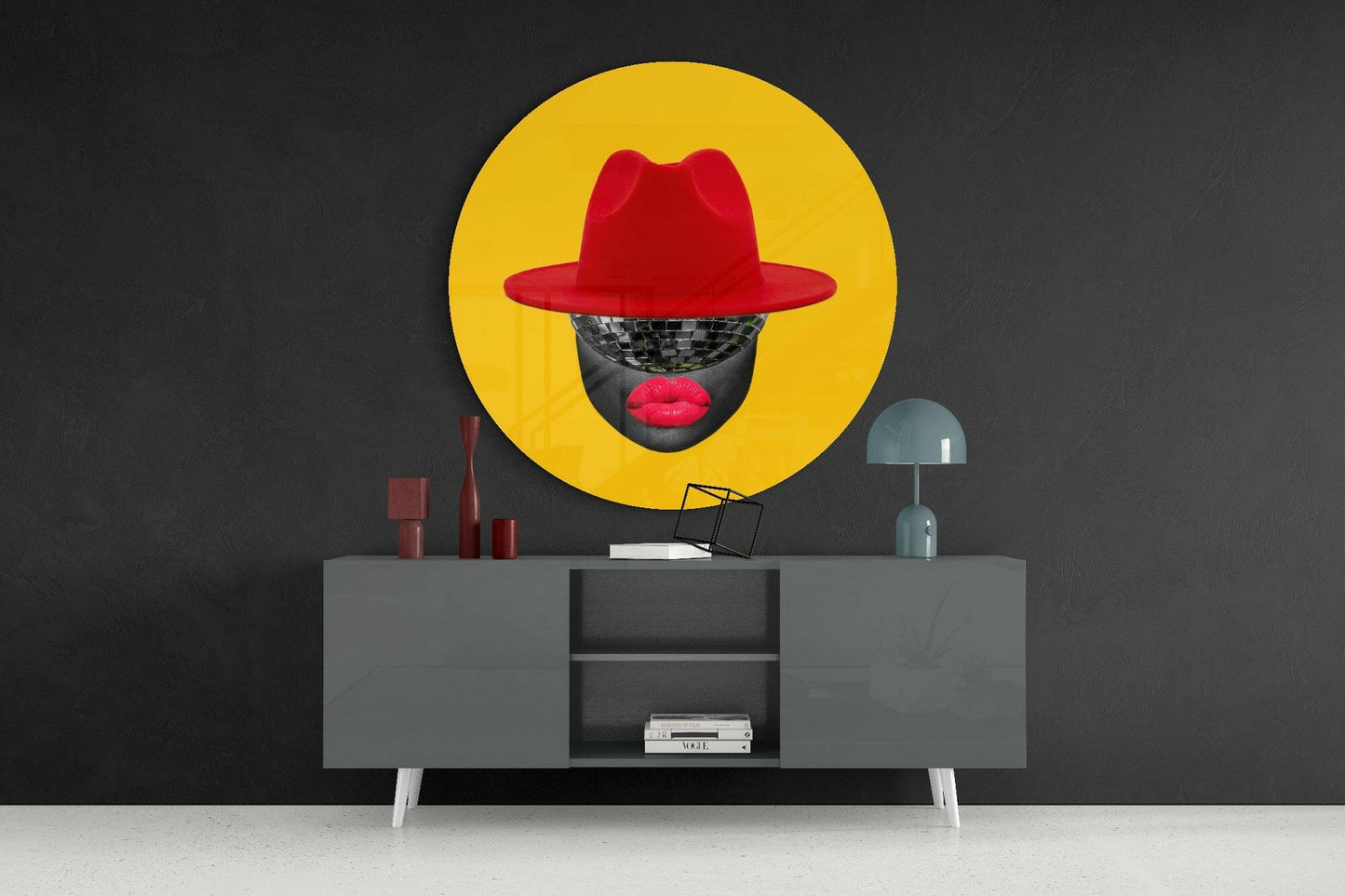 Yellow circular glass wall art with red hat and disco ball face displayed above gray mid-century modern console table.