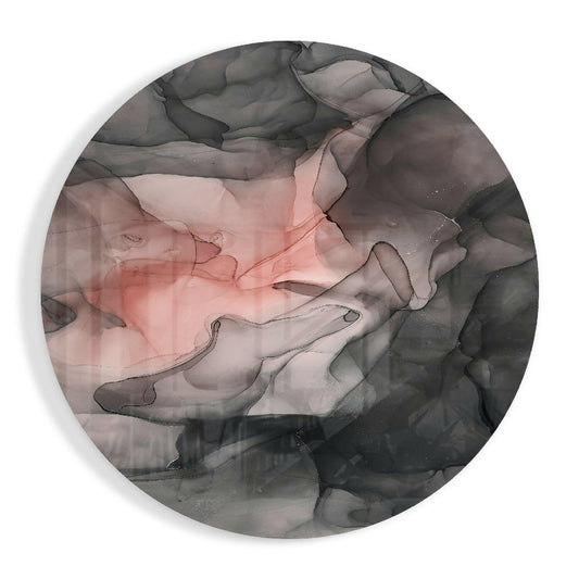 Circular glass wall art with black ink flowing across coral pink and gray watercolor washes, overhead view.
