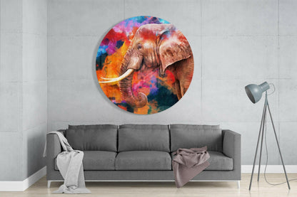 Colorful circular glass wall art depicting an elephant with vibrant orange, pink, and blue watercolor background, installed above a gray sofa in a modern living room.