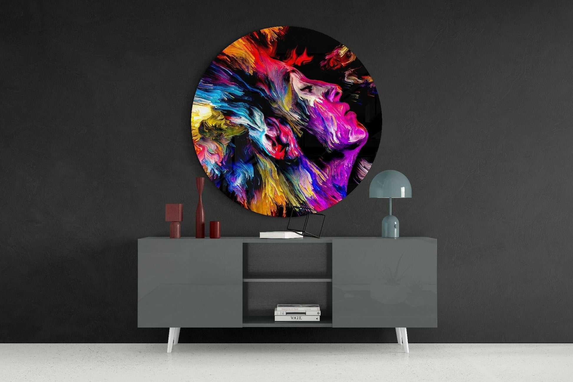 Colorful circular glass art featuring abstract painted portrait in vibrant hues mounted above gray modern credenza.