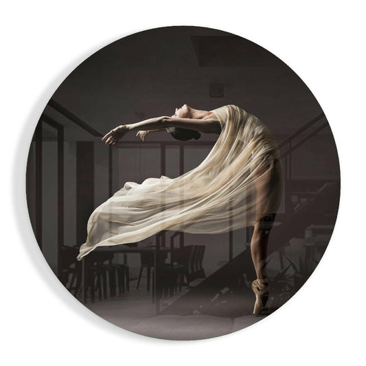 Ballerina in arabesque position wearing flowing cream silk veil against dark interior, circular glass art piece.