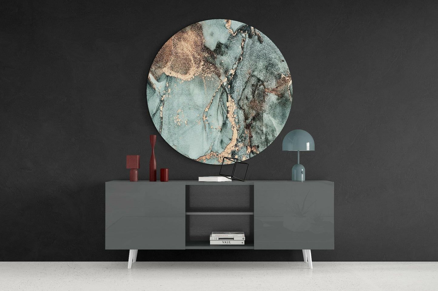 Round turquoise marble glass wall art displayed above gray sideboard with red candles and teal lamp against dark wall.
