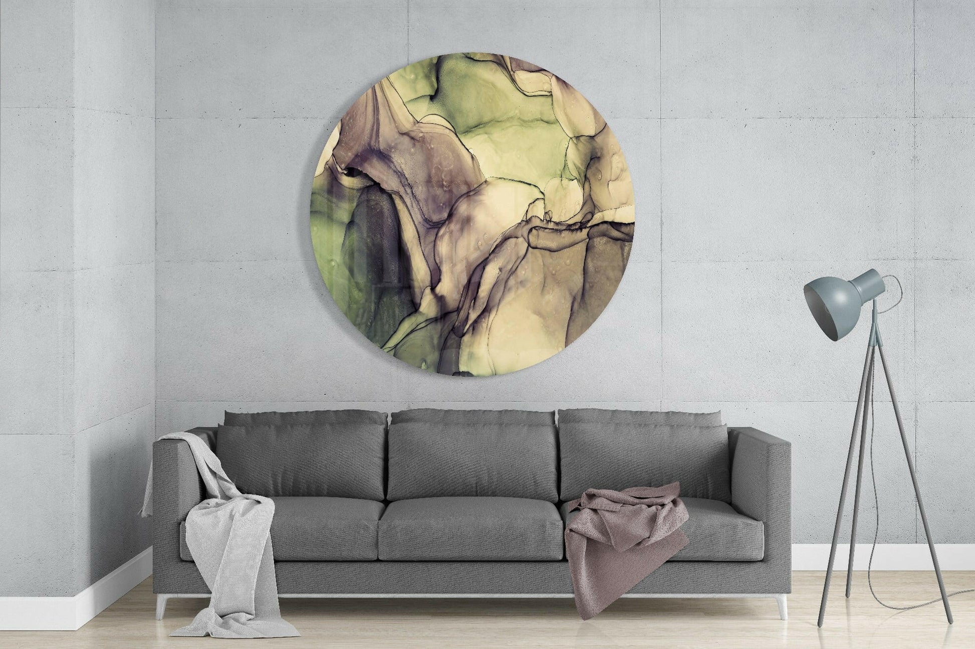 Round glass wall art with green and cream watercolor marble pattern displayed above gray sofa in modern living room interior.