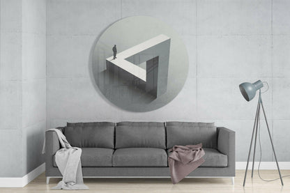 Circular glass wall art depicting an isometric labyrinth with a figure standing on white geometric platform, mounted above gray sofa in minimalist interior.