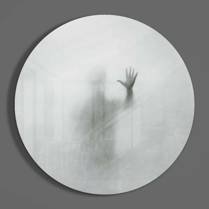 Blurred silhouette of a figure with raised hand visible through frosted white circular glass panel against gray background.