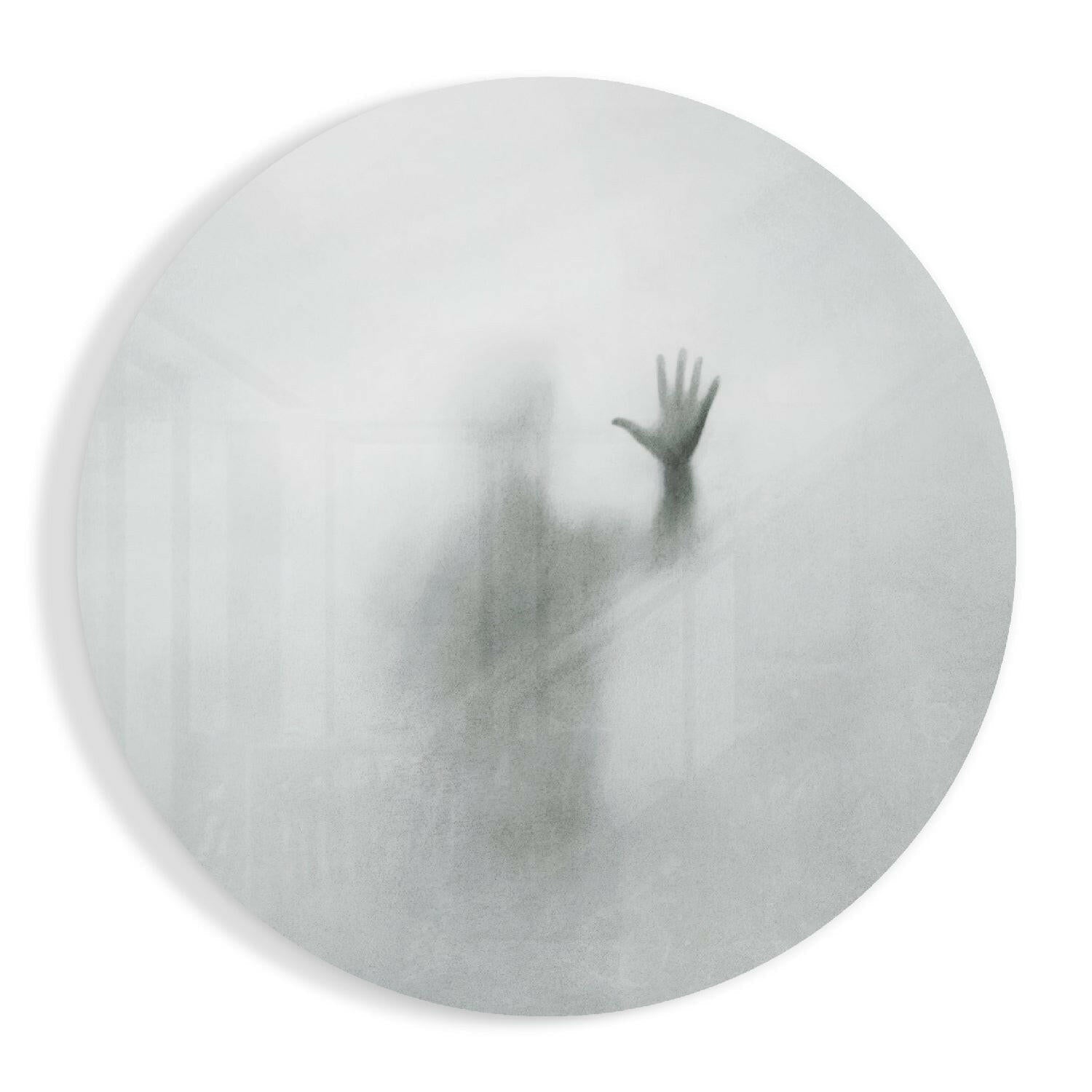 Frosted glass circular panel displaying a blurred silhouette of a person with raised arm against white background.