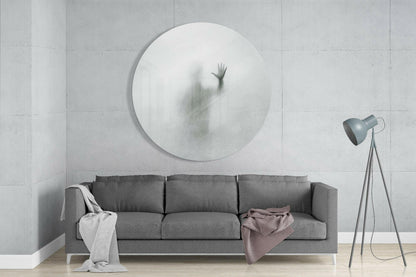 Large circular frosted glass wall art with blurred hand silhouette mounted above gray sofa in minimalist interior space.