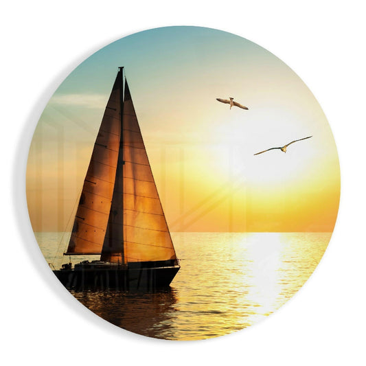 Silhouetted sailboat with amber sails on golden water at sunset, two birds flying overhead, circular glass art.