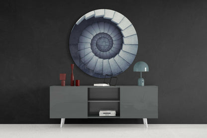 Circular stair glass wall art with concentric blue and grey tones displayed above a grey cabinet with red candles and green lamp.