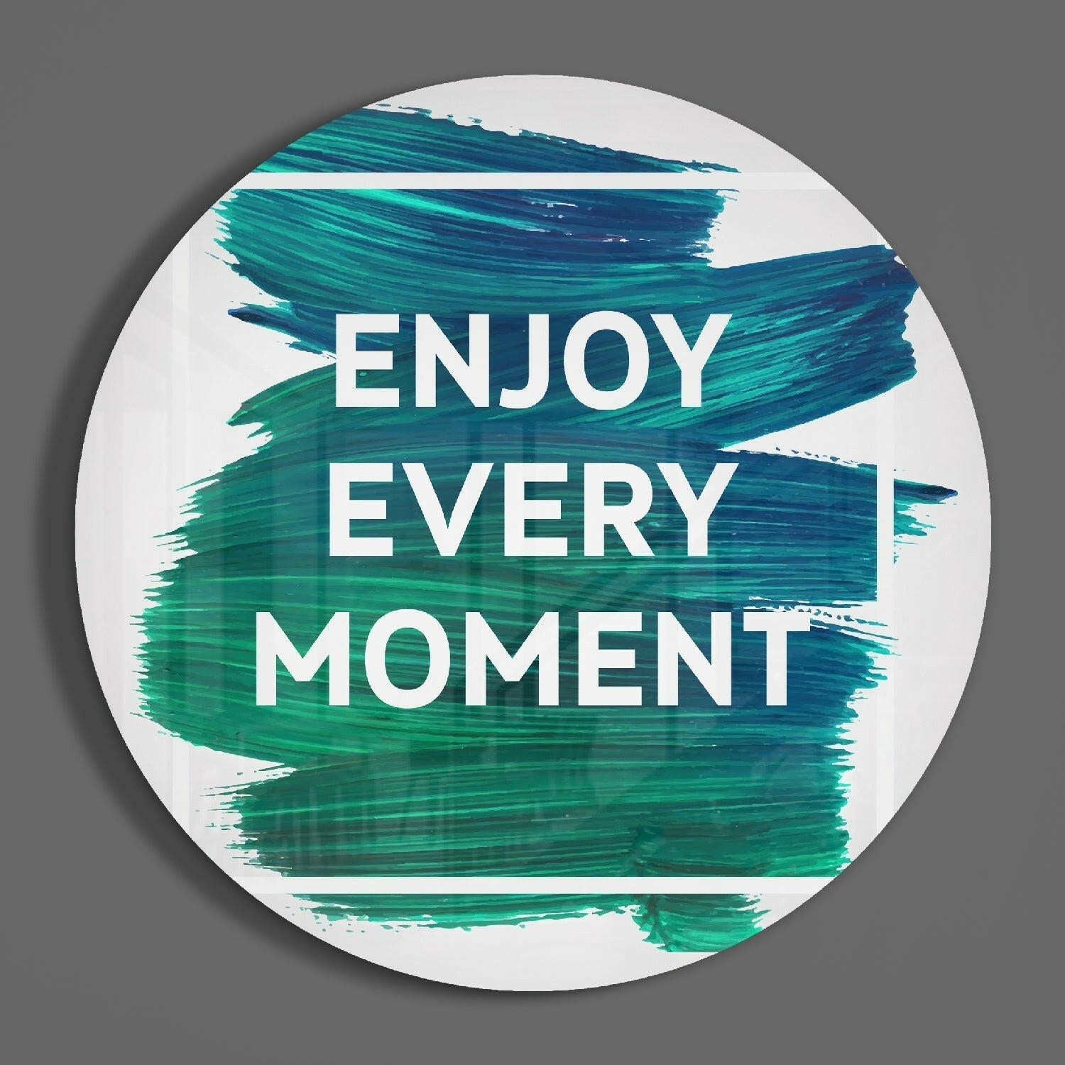 Round white glass wall art with teal and blue brushstroke design and white "ENJOY EVERY MOMENT" text, shown straight-on against gray background.