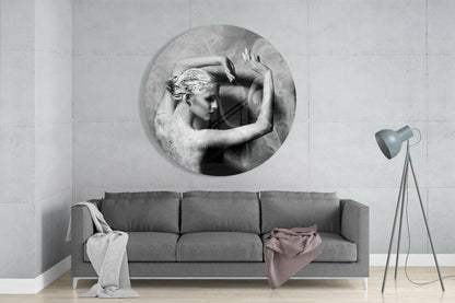 Round black and white glass wall art depicting a sculptural female figure above a gray sofa in a minimalist interior.