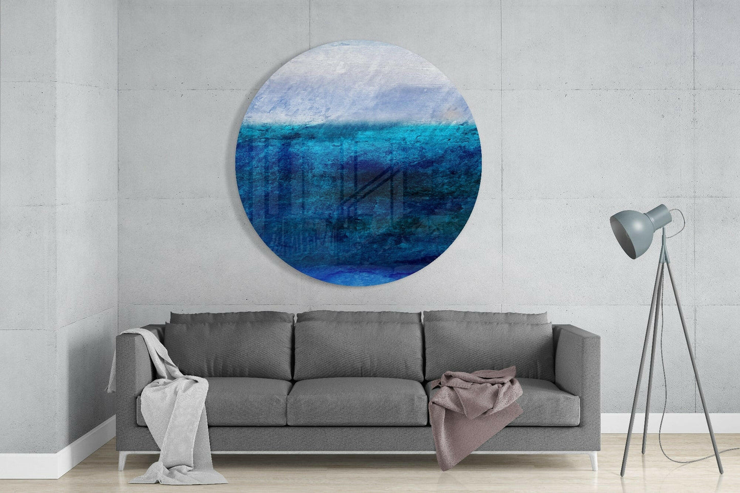 Round blue gradient glass artwork hung above gray sofa in minimalist interior with tripod lamp.