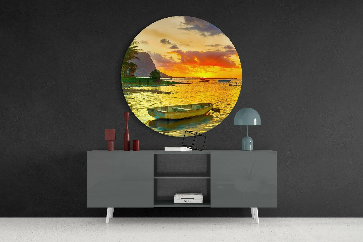 Circular glass wall art depicting a sunset coastal scene with moored boats, displayed above a gray console table with decorative accessories.