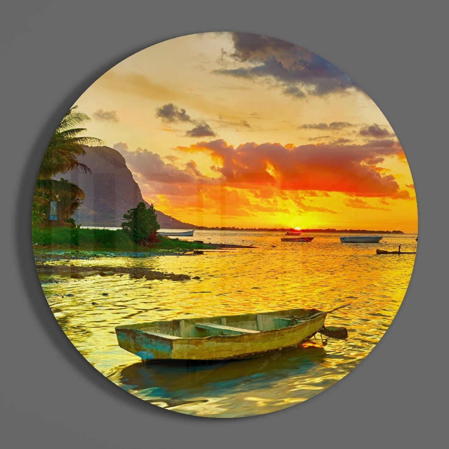 Weathered blue and green fishing boat in shallow golden water at sunset with palm trees and mountain backdrop on circular glass art.