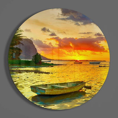 Weathered blue and green fishing boat in shallow golden water at sunset with palm trees and mountain backdrop on circular glass art.
