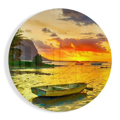Weathered blue and yellow rowboat floating in shallow golden water at sunset with palm trees and mountain backdrop on circular glass art.