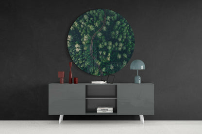 Circular aerial forest glass wall art with road displayed above gray sideboard with white legs against dark wall.