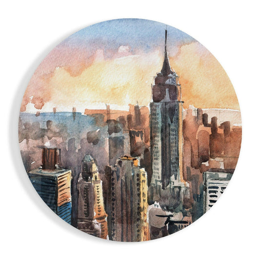 Watercolor painting of New York City skyline at sunset with warm orange and blue tones, featuring a prominent tall building in center, displayed on circular glass art piece.
