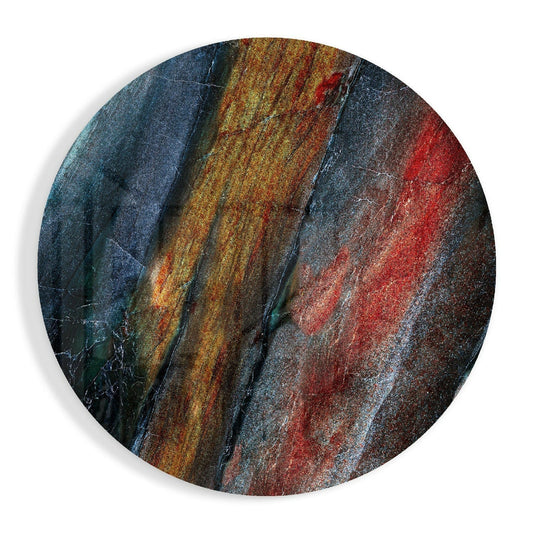 Circular glass wall art with diagonal striations in deep blue, golden yellow, and red mineral tones, displayed against white background.