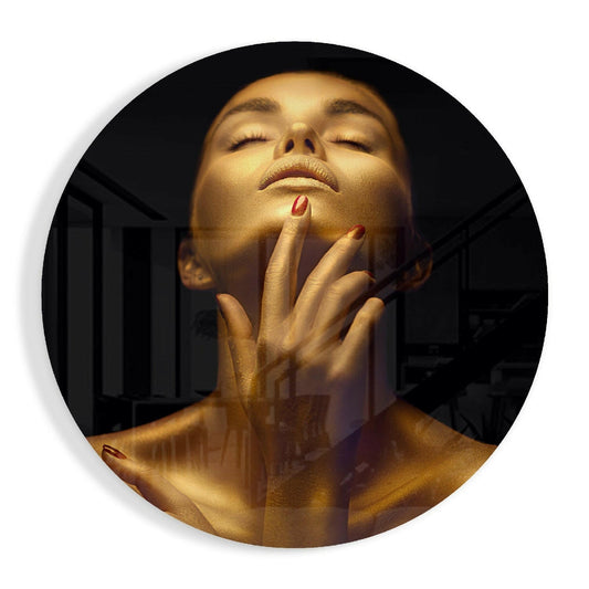 Woman with golden skin and closed eyes, hand touching chin, against dark background in circular glass art piece.