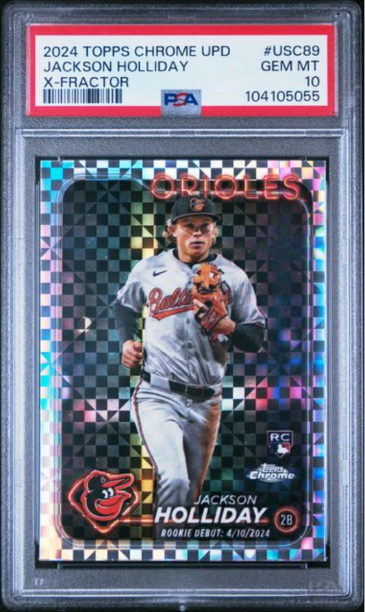 PSA-graded baseball card in clear case displaying Jackson Holliday in Orioles uniform against holographic X-factor background with colorful checkered border.