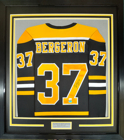 Framed Boston Bruins black jersey number 37 with "Bergeron" nameplate, signed, displayed front-facing in black frame with yellow and white borders.