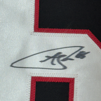 Close-up of embroidered signature on white jersey fabric with red and black trim borders.