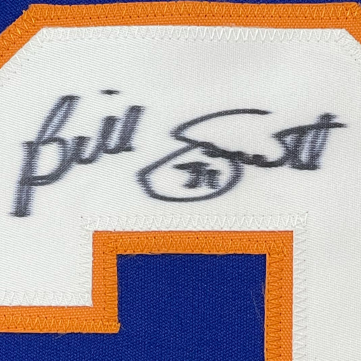 Close-up of handwritten signature on white jersey label with orange and blue borders.