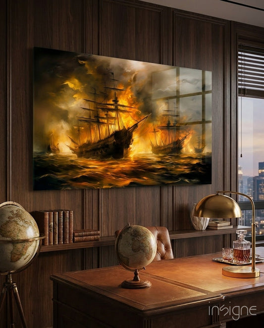 Dramatic glass wall art depicting burning sailing ships in golden flames, displayed above a wooden desk with globes and brass lamp in a dark wood-paneled office.