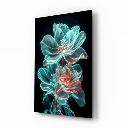 Angled view of a glass wall art panel displaying two neon-glowing flowers with cyan petals and coral-red centers against a black background.
