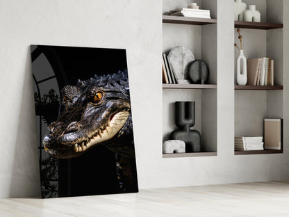 Glass art print leaning against white wall displaying crocodile's head with golden eye against black background, styled with shelving unit.