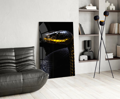 Black and yellow viper glass wall art displayed in modern living room beside grey leather chair and shelving unit.