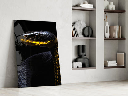 Black and yellow viper glass wall art leaning against white wall beside shelving unit displaying decorative objects and books.