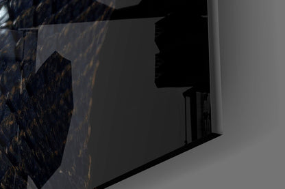 Close-up side view of black glass wall art with golden eye detail mounted on white wall surface.