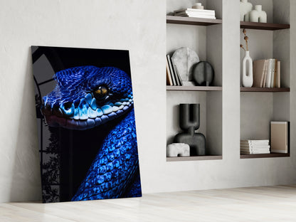 Blue viper glass wall art leaning against white wall beside shelving unit displaying decorative objects and books.