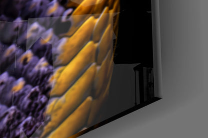 Close-up angled view of glass wall art showing purple and gold textured surface with black metal mounting bracket detail.