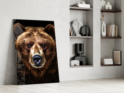 Glass wall art of a brown bear's frontal portrait against black background, leaning against white wall beside shelving unit.