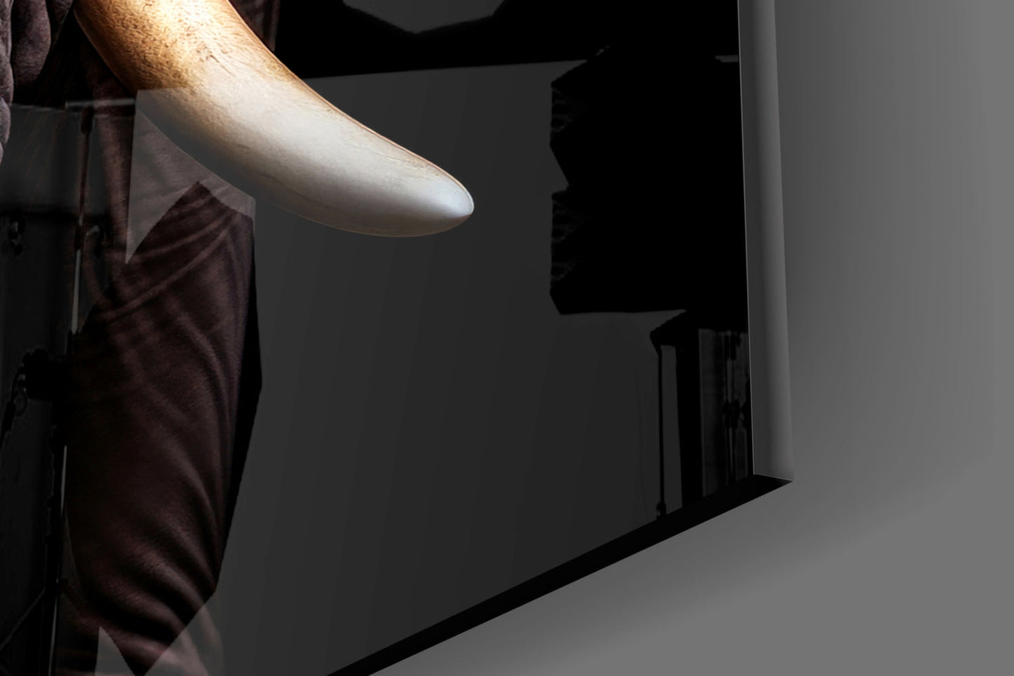 Close-up of a hand holding the edge of black glass wall art showing an elephant profile silhouette against gray wall.