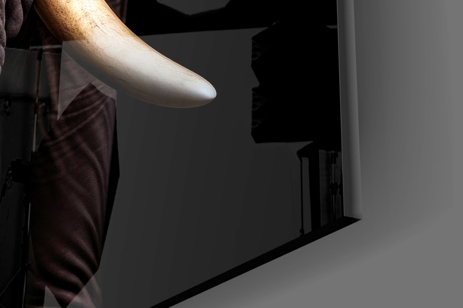 Close-up of a hand holding the edge of black glass wall art showing an elephant profile silhouette against gray wall.