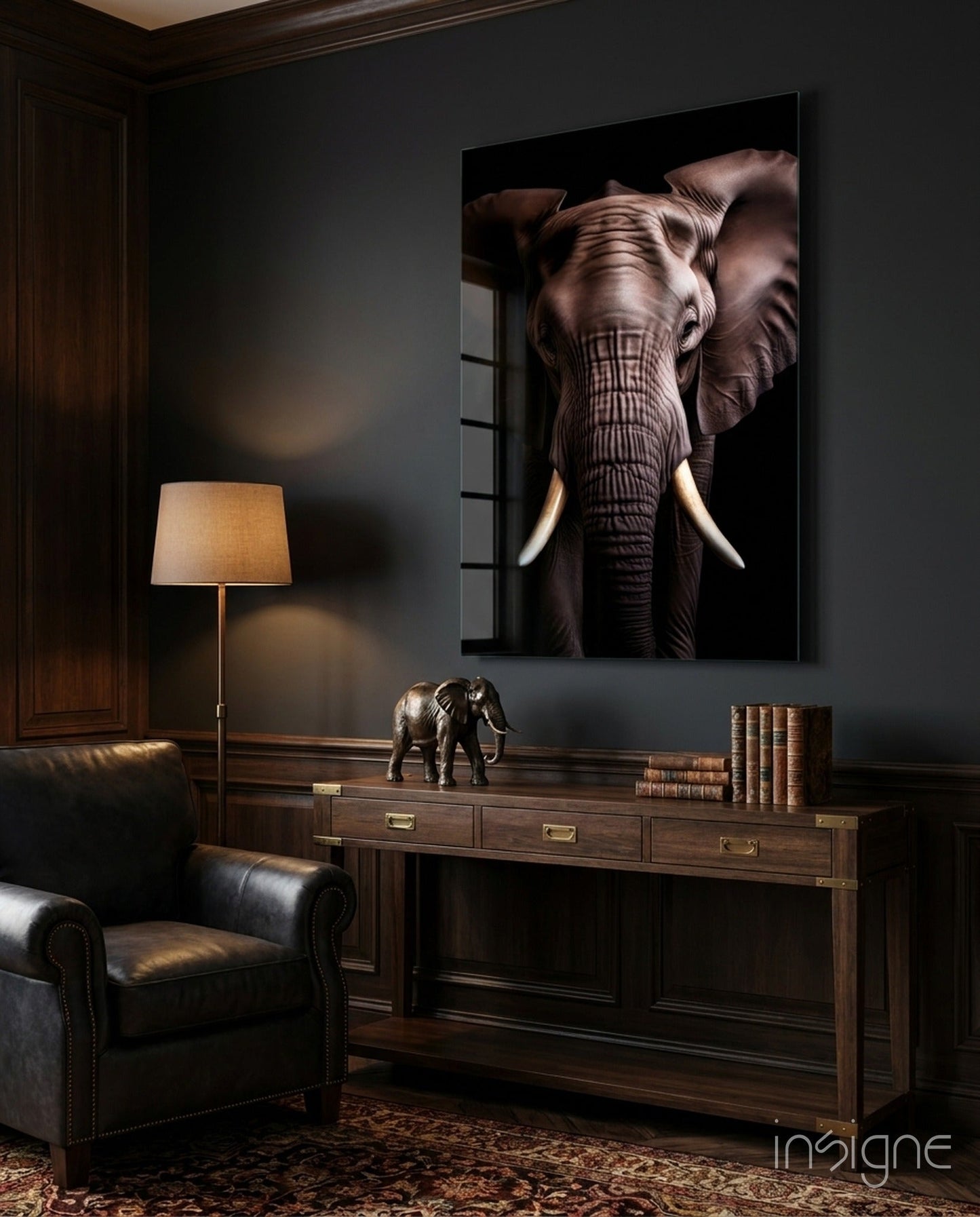 Large framed elephant portrait with ivory tusks hanging above wooden desk in dark study room with leather chair.
