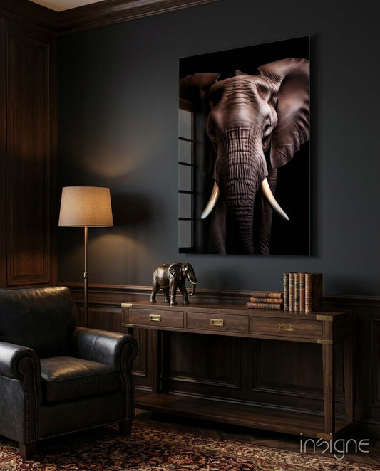 Large framed elephant portrait with ivory tusks hanging above wooden desk in dark study room with leather chair.
