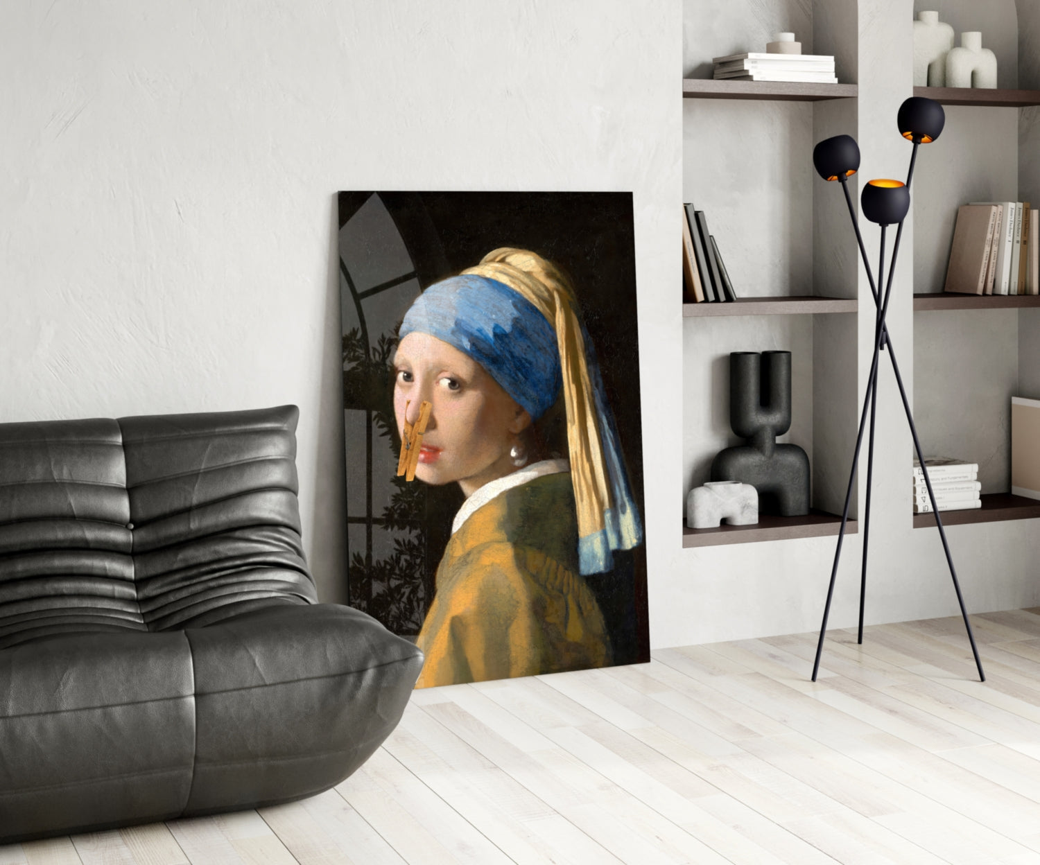 Girl with pearl earring and blue headwrap glass art leaning against wall in modern living room with black sofa and shelving.