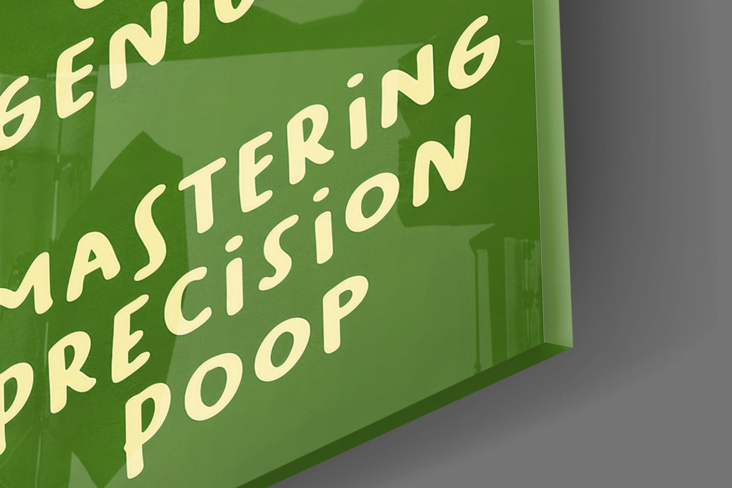 Close-up angled view of green glass wall art with pale yellow text reading "MASTERING PRECISION POOP," displayed against gray background.