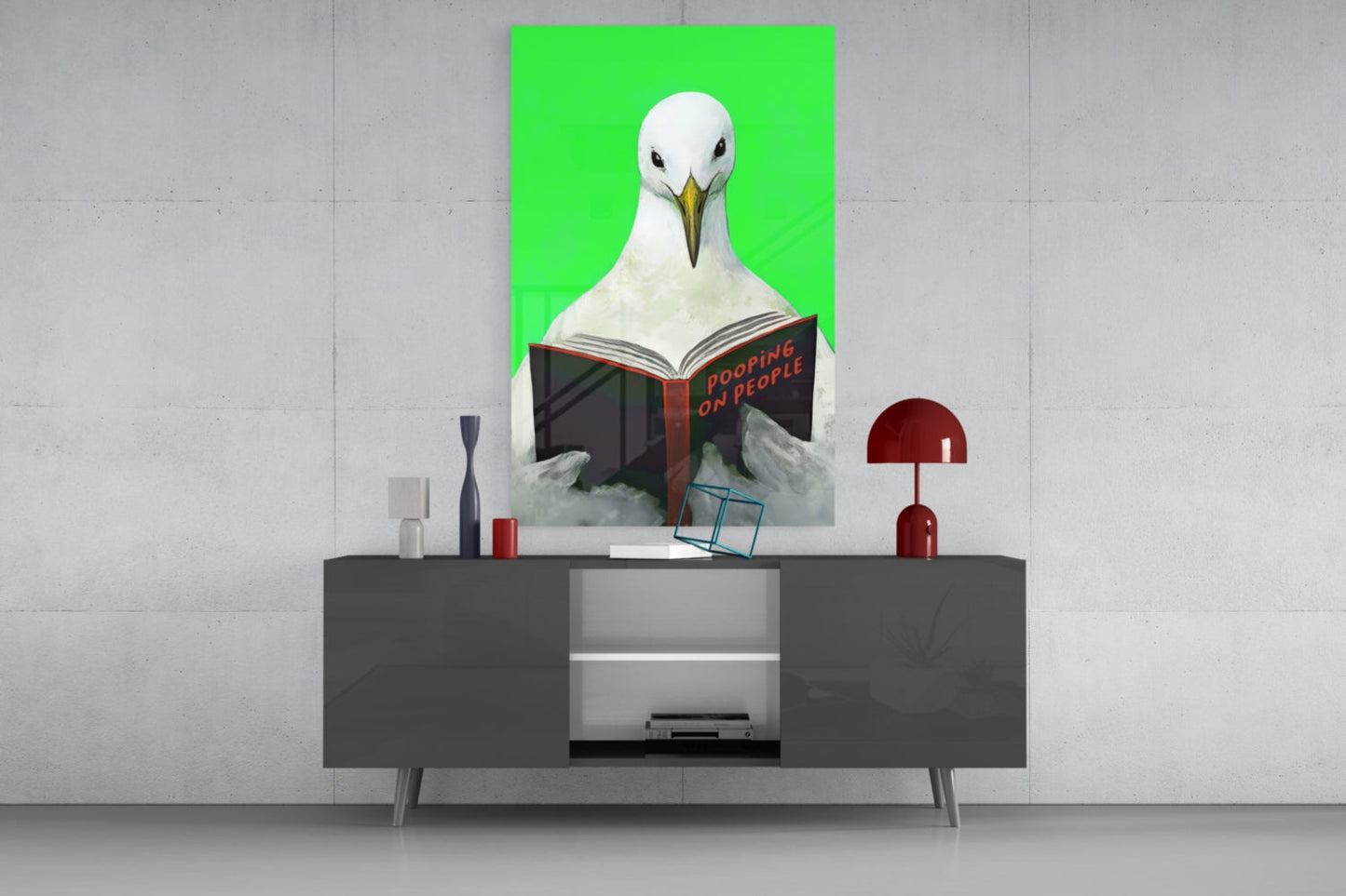 Seagull reading "Pooping on People" book on bright green background, displayed above gray media console with red lamp and decorative objects.